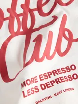 Remera blanca de manga corta, con corte holgado y diseño liso, cuenta con un pequeño estampado en el pecho con la leyenda "Coffee Club".