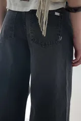 Pantalón jean gris oscuro de tiro medio y piernas anchas, con diseño de cinco bolsillos y cierre frontal con botón y cremallera.