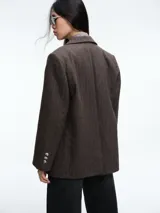 Blazer de corte sastrero color marrón con diseño de rayas verticales finas. Presenta solapas clásicas, cierre frontal de doble botonadura y un detalle de cadena metálica dorada en el bolsillo superior.