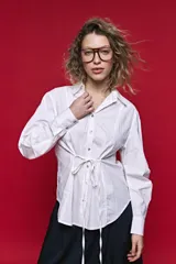 Camisa blanca de manga larga con volumen y estructura, cierre frontal con botones y lazo ajustable en la cintura que realza la silueta.