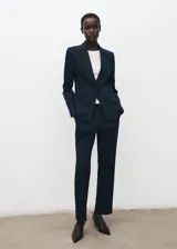 Blazer ajustado color azul marino, con cuello en V, solapas con muesca y cierre frontal de botones. Cuenta con bolsillos delanteros con solapa y bolsillo ribeteado en el pecho, mangas largas con puños abotonados, abertura en la parte trasera del bajo y forro interior.