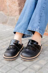 Mocasines negros de cuero con detalle de flecos en la parte delantera y suela gruesa con borde de corcho.