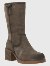 Bota de caña media confeccionada en cuero descarne, con diseño de punta redonda y taco cuadrado de altura media. Presenta costuras reforzadas en el empeine y un pequeño detalle metálico en la parte superior de la caña.