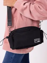 Riñonera negra de diseño rectangular con cierre frontal y compartimento principal. Presenta una etiqueta rectangular con el logo de la marca en el frente y correa ajustable con el nombre de la marca estampado.