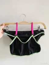 Conjunto de dos piezas compuesto por un top y una bombacha. El top es negro con ribetes en color verde claro y tirantes fucsias. La bombacha es negra con detalles en verde claro.
