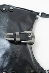 Bolso de hombro tipo baguette en color negro con acabado brillante. Presenta un diseño estructurado con una hebilla decorativa metálica en el frente y detalles de tachas plateadas en los laterales.