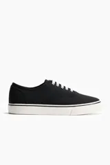 Calzado deportivo de lona de algodón en color negro con cordones blancos y suela de goma blanca con detalles en negro.