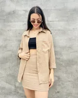 Camisa beige de manga larga con botones dorados y bolsillo en el pecho.