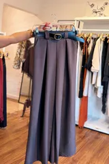 Pantalón de vestir beige de pernera ancha, con pinzas delanteras y bolsillos laterales. Incluye un cinto negro con hebilla metálica redonda.