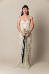 Vestido de novia strapless color natural, confeccionado en tul bordado con corsé drapeado y sobrefalda de tul. Presenta una faja con guarda en la cintura.