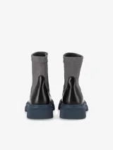 Bota estilo combat boot confeccionada en eco cuero negro con acabado mate y suela de goma azul. Presenta una caña alta de textura elastizada en color gris y cierre lateral.