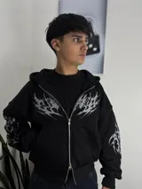 Campera con capucha y cierre frontal, color negro con estampado tribal en color gris en el pecho y las mangas. Presenta un corte boxy y holgado.