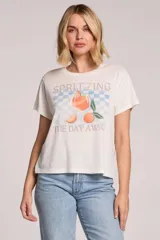 Remera blanca de algodón y poliéster, con cuello redondo y diseño holgado. Cuenta con un estampado frontal de inspiración vintage con la frase "Spritzing the day away", un fondo de tablero a cuadros en tonos celestes y la ilustración de una copa de spritz junto a naranjas y hojas.