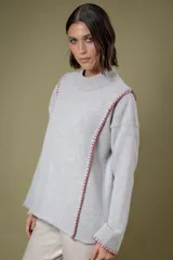 Buzo de lana gris con cuello alto y corte holgado. Presenta detalles de costuras decorativas en color rojo a lo largo de los hombros y el frente.