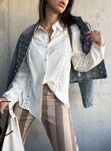 Camisa blanca de manga larga con detalles de encaje y calados verticales en el frente y las mangas.