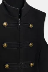 Chaleco negro de cuello subido y manga sisa, con cierre frontal oculto y detalle de botones decorativos metálicos en estilo militar.