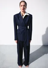 Pantalón de traje tiro medio, corte recto y largo, con diseño de raya diplomática, pinzas y bolsillos laterales.