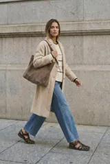 Tapado largo de corte oversize en color beige, con solapas clásicas y cierre frontal con botones. Presenta un diseño minimalista y elegante, ideal para un look sofisticado.