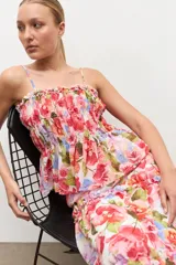 Top de tirantes finos con escote recto y detalle fruncido con elástico en el pecho. Presenta diseño con volados escalonados y estampado floral color rosado.