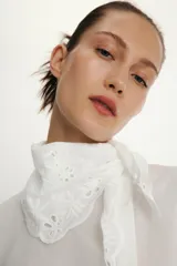 Camisa de manga larga en color blanco, confeccionada con detalles de bordados perforados a tono. Presenta un cuello tipo pañuelo y cierre frontal con botones.