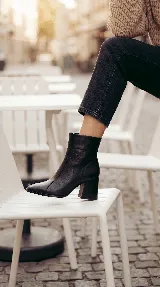 Bota corta de cuero negro con taco cuadrado y punta cuadrada. Presenta un diseño minimalista con costura central vertical y caña media.