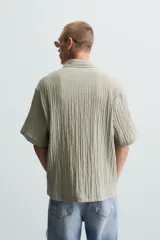 Camisa de manga corta con cuello solapa, confeccionada en tejido de mezcla de lyocell con textura de efecto arrugado y cierre frontal de botones.