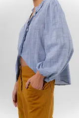 Camisa de manga larga color beige con diseño a rayas sutiles, cuello mao con volados y abertura frontal con detalles de volados a un lado.
