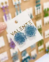Par de caravanas con diseño floral de resina traslúcida en color azul con destellos de glitter incorporados.