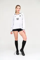 Camiseta blanca de manga larga con cuello en V y detalles en negro. Presenta el logo de la marca en el pecho, el número 92 y un escudo con tres balones de fútbol.