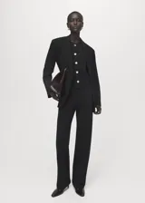 Chaleco de punto fino color negro, con cuello redondo, diseño recto sin mangas y cierre frontal de botones dorados.
