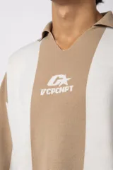 Sweater de punto con diseño a rayas verticales en color beige y blanco, de corte holgado y cuello polo abierto. Presenta un logo bordado en el centro del pecho.