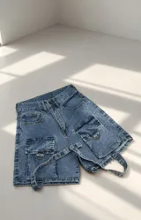 Short de denim azul con bolsillos cargo laterales y tiras decorativas con argollas metálicas.