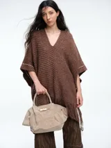 Poncho tejido de punto grueso color marrón, con escote en V, diseño amplio y flecos en el ruedo. Presenta detalles de costuras decorativas en los laterales.