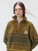 Pullover de punto con textura aterciopelada, diseño oversize, cuello polo con cierre frontal parcial y detalles de pespuntes en contraste. Presenta rayas horizontales en tonos tierra y un parche bordado con la letra M en el pecho.