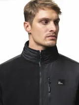 Campera de polar negro con cuello alto y cierre frontal completo. Presenta paneles de nylon en contraste en el pecho, hombros y codos, incluyendo un bolsillo vertical con cierre en el pecho y dos bolsillos laterales abiertos.