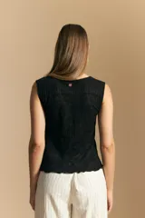 Top sin mangas de jacquard color negro, con cuello cerrado y silueta recta. Presenta una textura trabajada con relieve y una terminación suavemente ondulada en el ruedo.