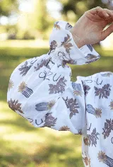 Camisa de lino con estampado floral y tipográfico, cuello alto con volados, cierre frontal con botones y mangas largas abullonadas con puños elásticos.