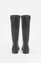 Bota de montar de caña alta color negro, con suela track y detalle de tira con hebilla metálica dorada en la parte superior de la caña.