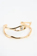 Brazalete abierto dorado de diseño orgánico con doble banda y aplicación de cristal central en forma de ojo.