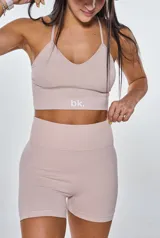 Conjunto deportivo compuesto por un top con espalda de tiras cruzadas y un short de tiro alto con efecto fruncido en la parte trasera. Ambas piezas son de color beige y presentan un diseño ajustado sin costuras.