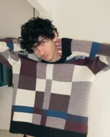 Sweater de cuello redondo con diseño jacquard a cuadros en tonos azul, marrón, blanco y negro. Presenta un ajuste holgado y puños, cuello y ruedo acanalados.