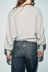 Chaqueta de punto color beige claro, de cuello redondo y manga larga abullonada con puño ajustado. Cierre frontal cruzado con botones plateados.