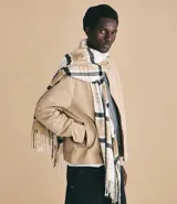 Bufanda de punto suave con estampado de cuadros en tonos beige, blanco y negro, con terminaciones de flecos en los extremos.