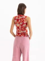 Top al cuerpo sin mangas con escote alto tipo polera y detalle de frunce en el centro delantero. Presenta un estampado full print de flores hibiscos en tonos rojos y naranjas sobre base celeste.