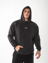 Canguro con capucha de felpa premium, color negro con efecto lavado a la piedra. Presenta un diseño oversize unisex con la frase 'STAY PRESENT HERE AND NOW' bordada en la espalda.