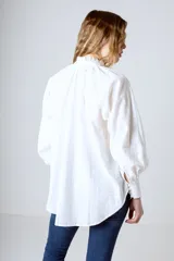 Blusa blanca de algodón con cuello alto con volantes y botonadura frontal parcial. De manga larga con puños abullonados.