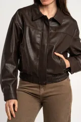 Campera bomber de cuero sintético marrón, con cierre frontal, cuello camisero, bolsillos laterales y elástico en los puños y la cintura.