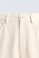 Bermuda de algodón color beige claro, de corte relajado y largo hasta la rodilla. Presenta cierre frontal con cremallera y botón, bolsillos delanteros y bolsillo cerillero, además de bolsillos traseros de plastrón.