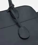 Cartera modelo stachel de tamaño grande, confeccionada en poliuretano color negro. Presenta asas cortas, cierre superior con botón a presión y detalles metálicos decorativos.