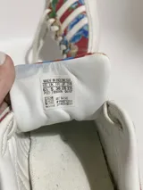 Championes Adidas modelo Superstar, con diseño estampado floral en tonos azules, rojos y amarillos sobre base de tela, con la clásica puntera de goma blanca y cordones blancos.